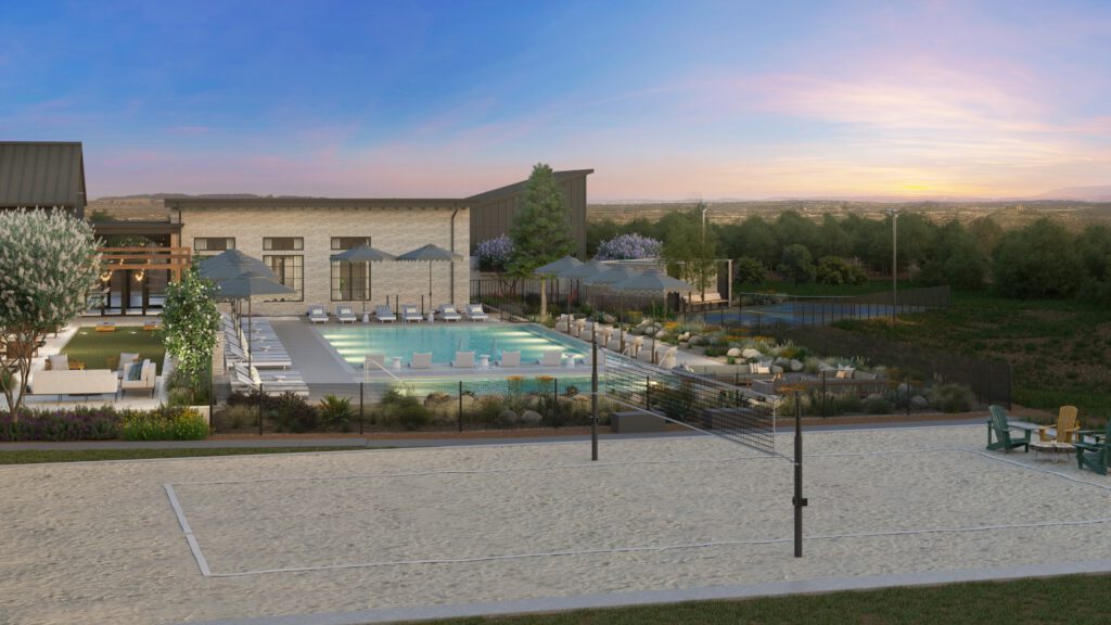 Sand volleyball court in the foreground with an outdoor pool, lounge areas, and expansive landscape views in the background