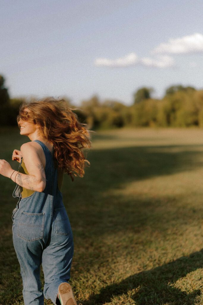 Woman running in a field with flowing hair and overalls